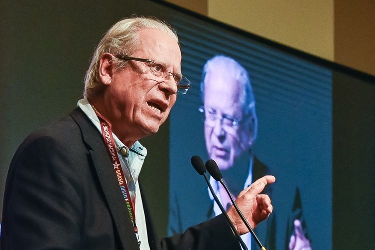 José Dirceu discursando em evento político, expressando seriedade.