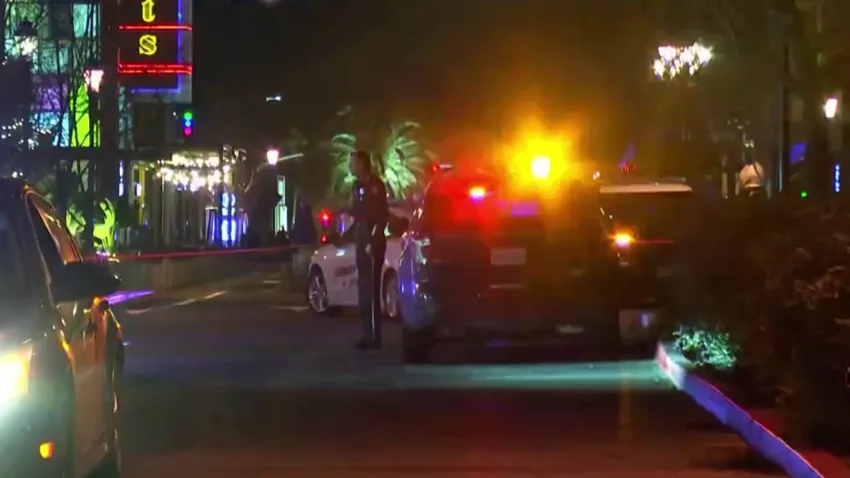 rea isolada pela polícia em Santana Row, San Jose, com mesas de café vazias e viaturas ao fundo após o ataque.