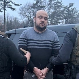 Agentes do ICE realizando operação de custódia em Massachusetts; viatura oficial ao fundo.