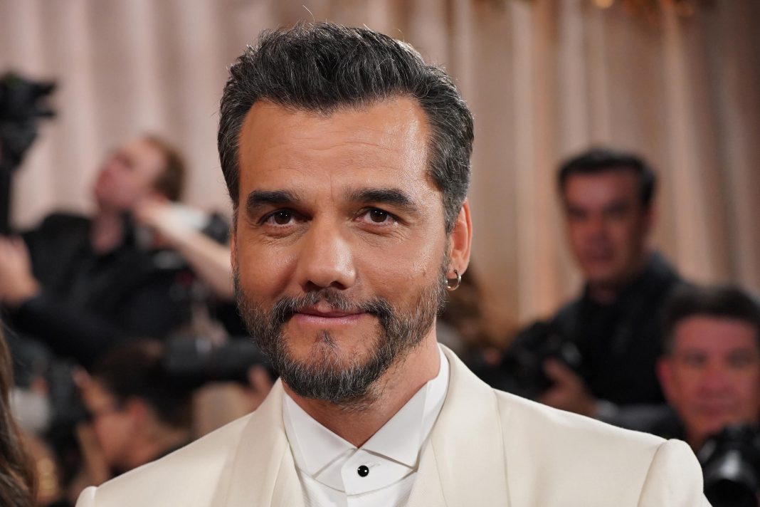 Ator Wagner Moura em um tapete vermelho, com expressão séria, durante premiação de cinema internacional.