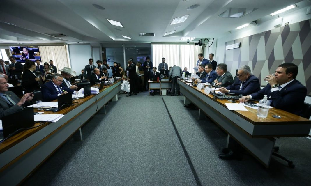 Fotografia do painel do Congresso Nacional durante sessão da CPMI com parlamentares discutindo o relatório final.