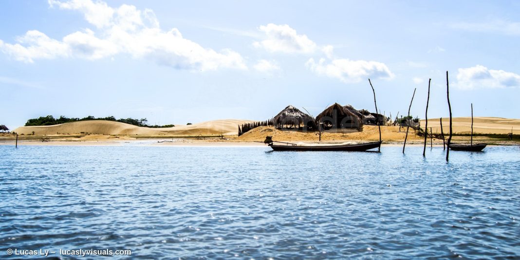 Crianças em área rural de Barreirinhas atravessando água com mochilas protegidas por baldes plásticos.