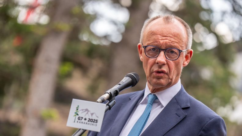 O chanceler da Alemanha, Friedrich Merz, discursando em um púlpito oficial com a bandeira alemã ao fundo.