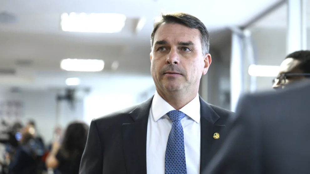 senador Flávio Bolsonaro gesticulando durante pronunciamento político, com fundo em tons escuros e iluminação focada.